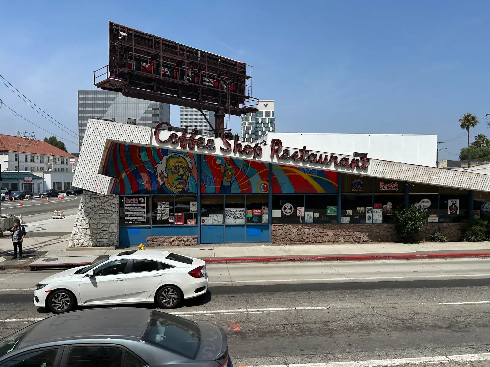 Johnie's Coffee Shop on Wilshire Boulevard in Los Angeles, a 1956 Googie building with a sharply angled roof, stone walls and a large "Coffee Shop Restaurant" sign, repainted with a colorful mural.